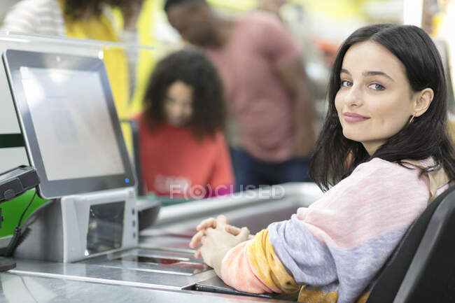 Retrato confiante jovem caixa feminina trabalhando no checkout no supermercado — Fotografia de Stock