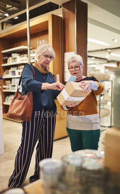 Mujeres mayores con compras de teléfonos inteligentes en casa buena tienda - foto de stock