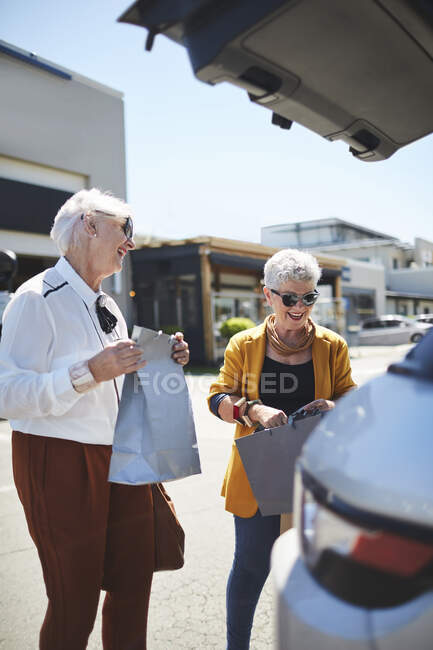 Heureuses femmes âgées amis chargement de sacs à provisions à l'arrière du SUV dans le stationnement du centre commercial — Photo de stock