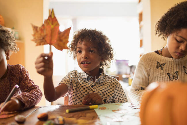 Menino curioso segurando folha de outono na mesa — Fotografia de Stock
