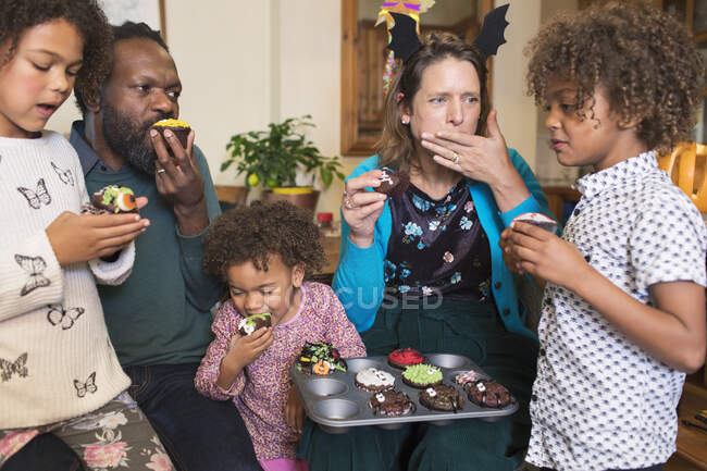 Familia multiétnica comiendo cupcakes de Halloween decorados - foto de stock