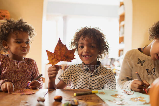 Retrato menino feliz com folha de outono fazendo artesanato com irmãs à mesa — Fotografia de Stock
