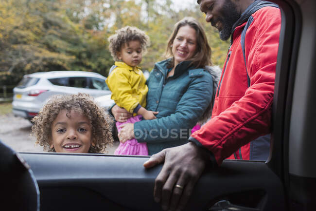 Retrato niño sonriente de pie fuera del coche con la familia - foto de stock