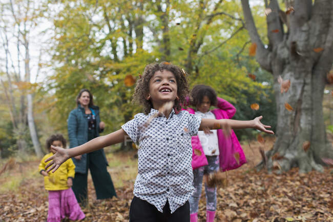Menino despreocupado brincando em folhas de outono com a família na floresta — Fotografia de Stock