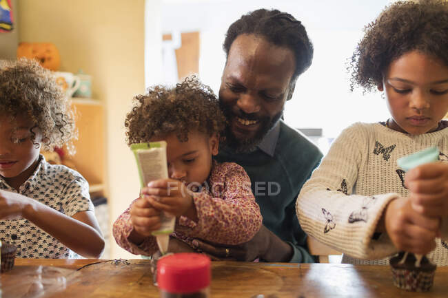 Pai e crianças decorando cupcakes com geada à mesa — Fotografia de Stock