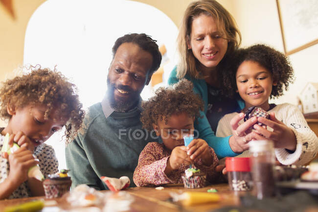 Família multiétnica que decora cupcakes à mesa — Fotografia de Stock