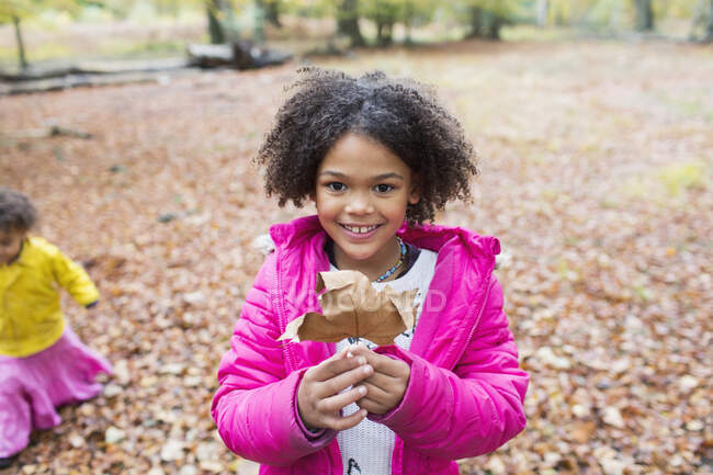 Portrait happy girl holding autumn leaf in woods — Stock Photo