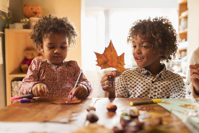 Hermano y hermana haciendo artesanías con hojas de otoño en la mesa - foto de stock