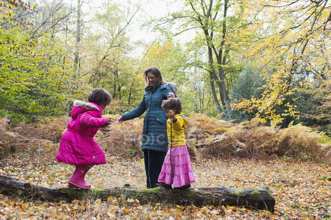 Mother and daughters playing on fallen log in autumn woods — Stock Photo