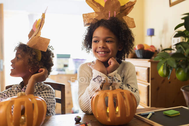 Happy girl in turkey hat carving pumpkin at table — Stock Photo