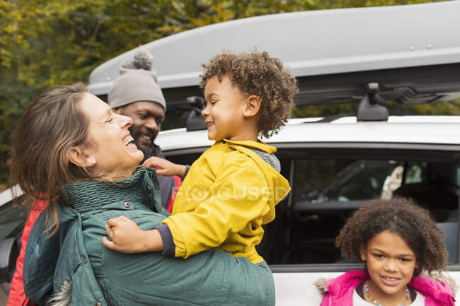 Happy family hugging outside car in parking lot — Stock Photo