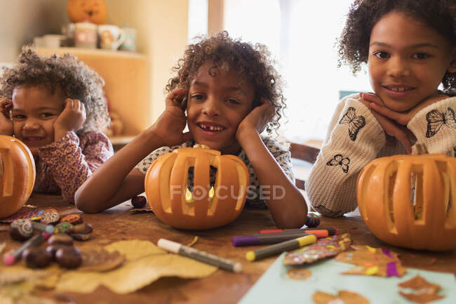 Retrato feliz hermano y hermanas tallando calabazas en la mesa - foto de stock
