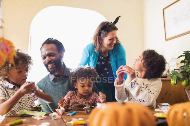 Happy family decorating Halloween cupcakes at table — Stock Photo