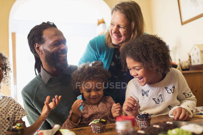 Happy multiethnic family decorating Halloween cupcakes at table — Stock Photo