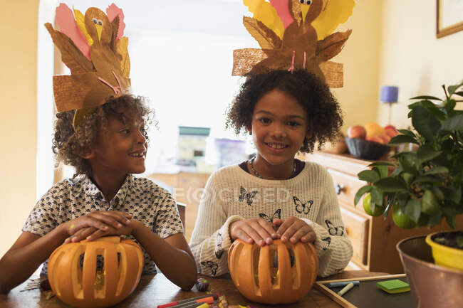 Retrato feliz hermano y hermana con sombreros de pavo tallando calabazas - foto de stock