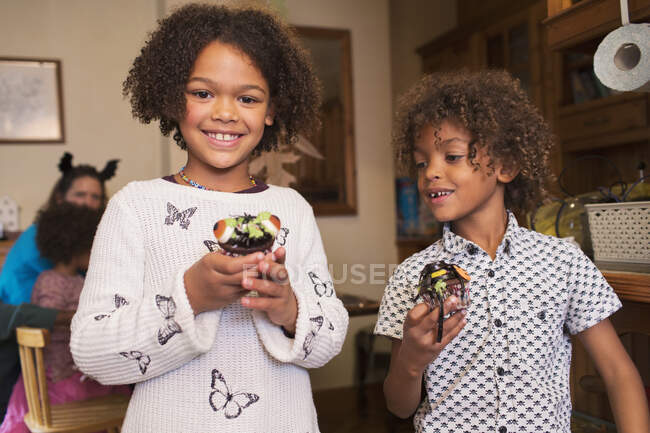 Portrait happy brother and sister with decorated Halloween cupcakes — Stock Photo