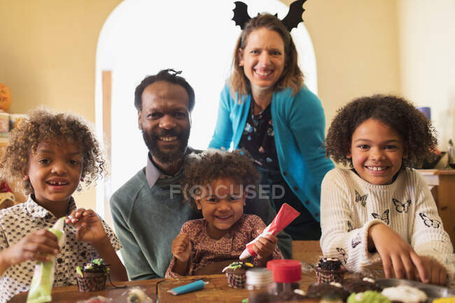 Retrato feliz familia decoración de Halloween cupcakes en la mesa - foto de stock