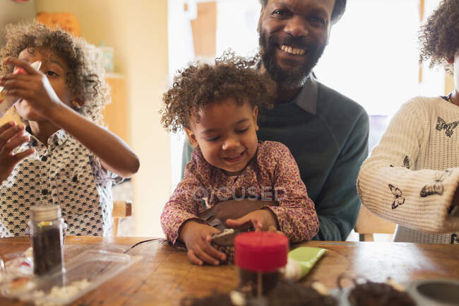 Счастливый отец и дети украшают кексы за столом — стоковое фото