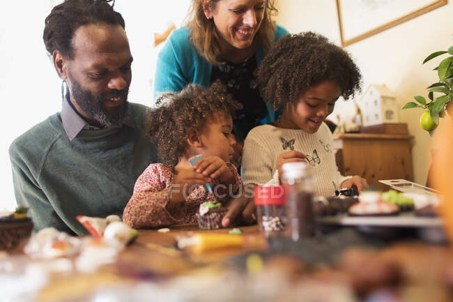 Family decorating cupcakes at table — Stock Photo