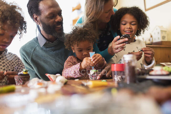 Multiethnic family decorating cupcakes at table — Stock Photo