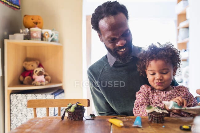 Счастливые отец и дочь украшать Хэллоуин кексы за столом — стоковое фото