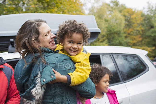 Retrato feliz madre sosteniendo hija fuera de coche en el estacionamiento - foto de stock
