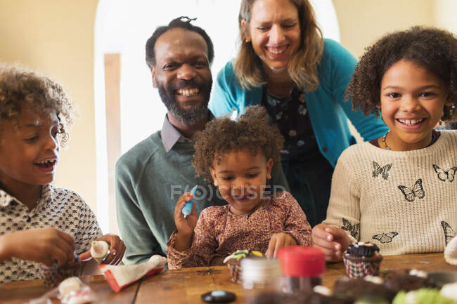 Portrait of happy multiethnic family decorating cupcakes at table — Stock Photo