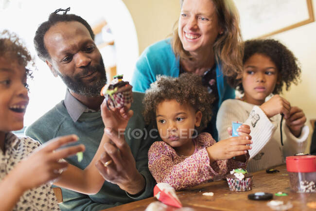 Happy famille multiethnique décoration cupcakes à table — Photo de stock