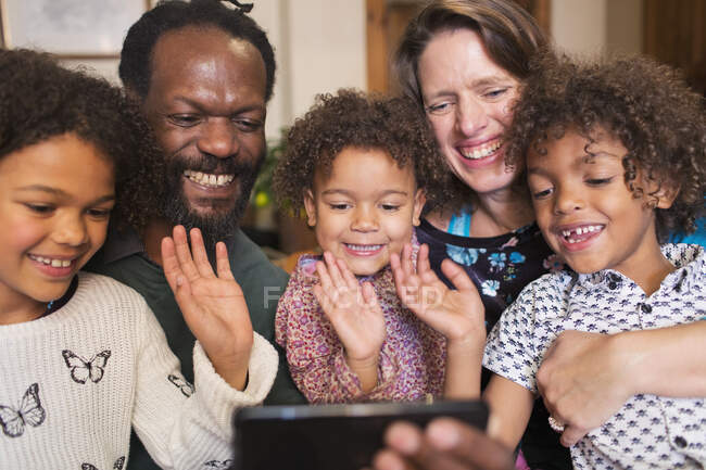 Familia multiétnica feliz saludando y chat de vídeo con el teléfono inteligente - foto de stock