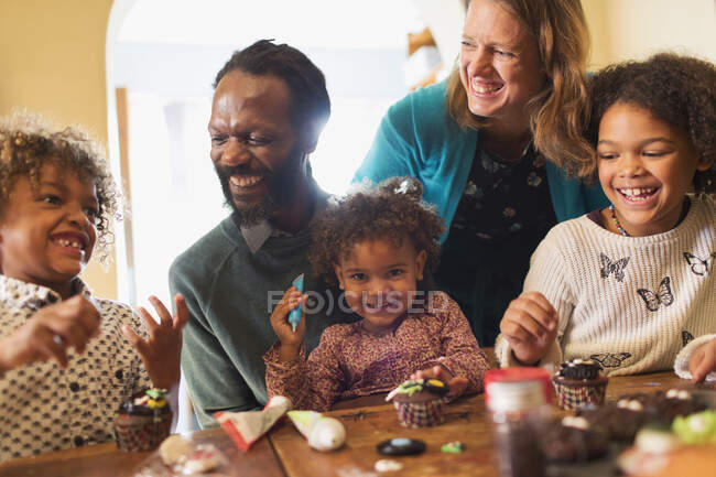 Счастливая многонациональная семья украшать кексы за столом — стоковое фото