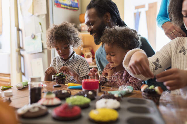 Familie dekoriert Halloween-Cupcakes am Tisch — Stockfoto