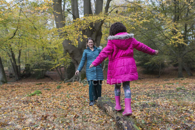 Mother and daughter balancing on fallen log in autumn woods — Stock Photo