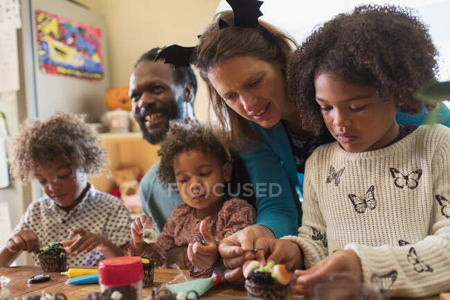 Familia multiétnica decorando cupcakes de Halloween en la mesa - foto de stock