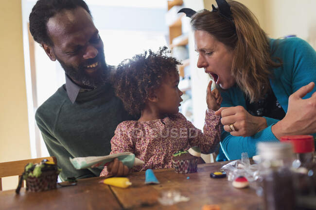 Glückliche multiethnische Familie dekoriert Halloween-Cupcakes am Tisch — Stockfoto