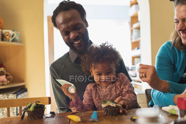 Happy family decorating Halloween cupcakes at table — Stock Photo