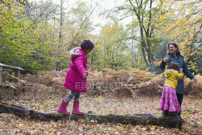 Mother and daughters walking on fallen log in autumn woods — Stock Photo