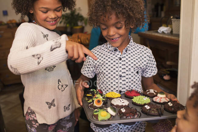 Happy brother and sister with decorated Halloween cupcakes — Stock Photo