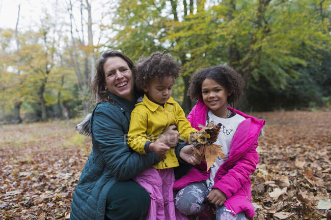 Retrato feliz madre e hijas jugando en otoño hojas en el bosque - foto de stock