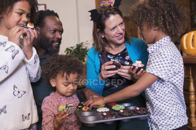 Familia multiétnica comiendo cupcakes de Halloween decorados - foto de stock