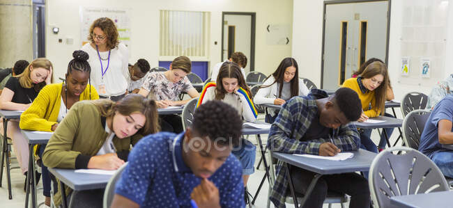 Insegnante di scuola superiore supervisionare gli studenti sostenere l'esame alle scrivanie — Foto stock