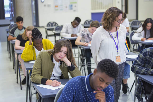 High school teacher supervising students taking exam desks classroom — Stock Photo