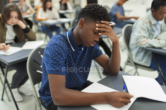 Focused liceale ragazzo prendendo esame a scrivania in aula — Foto stock