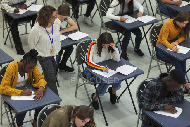Profesora de secundaria supervisando estudiantes que toman exámenes en las mesas - foto de stock