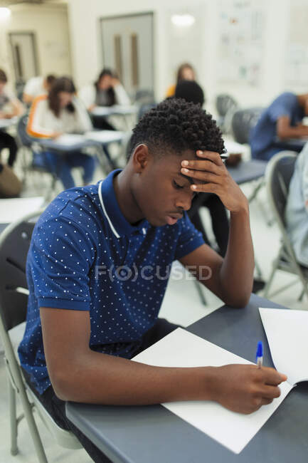 Focused liceale ragazzo studente presa esame a scrivania in aula — Foto stock