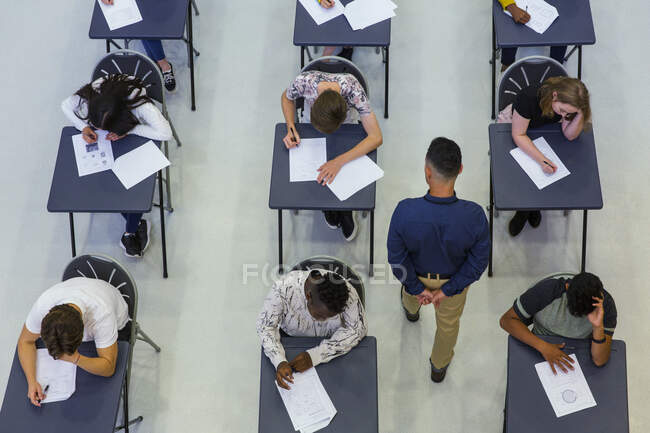 Учитель старшей школы, курирующий студентов, сдающих экзамен за партами — стоковое фото