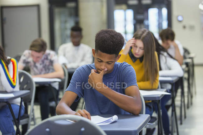 Estudiante de secundaria enfocado tomando examen en el escritorio en el aula - foto de stock