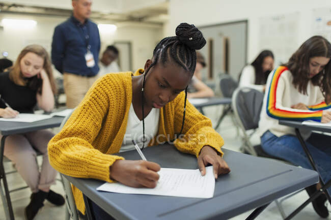 Сосредоточенная ученица старшей школы, сдающая экзамен за столом — стоковое фото