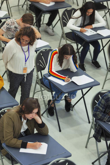 Викладач середньої школи контролює студентів, які складають іспит за столами — стокове фото