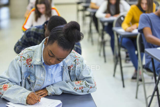 Estudiante de secundaria enfocada tomando examen en el escritorio en el aula - foto de stock