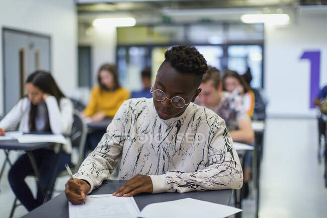 Сосредоточенный ученик старшей школы, сдающий экзамен за столом в классе — стоковое фото